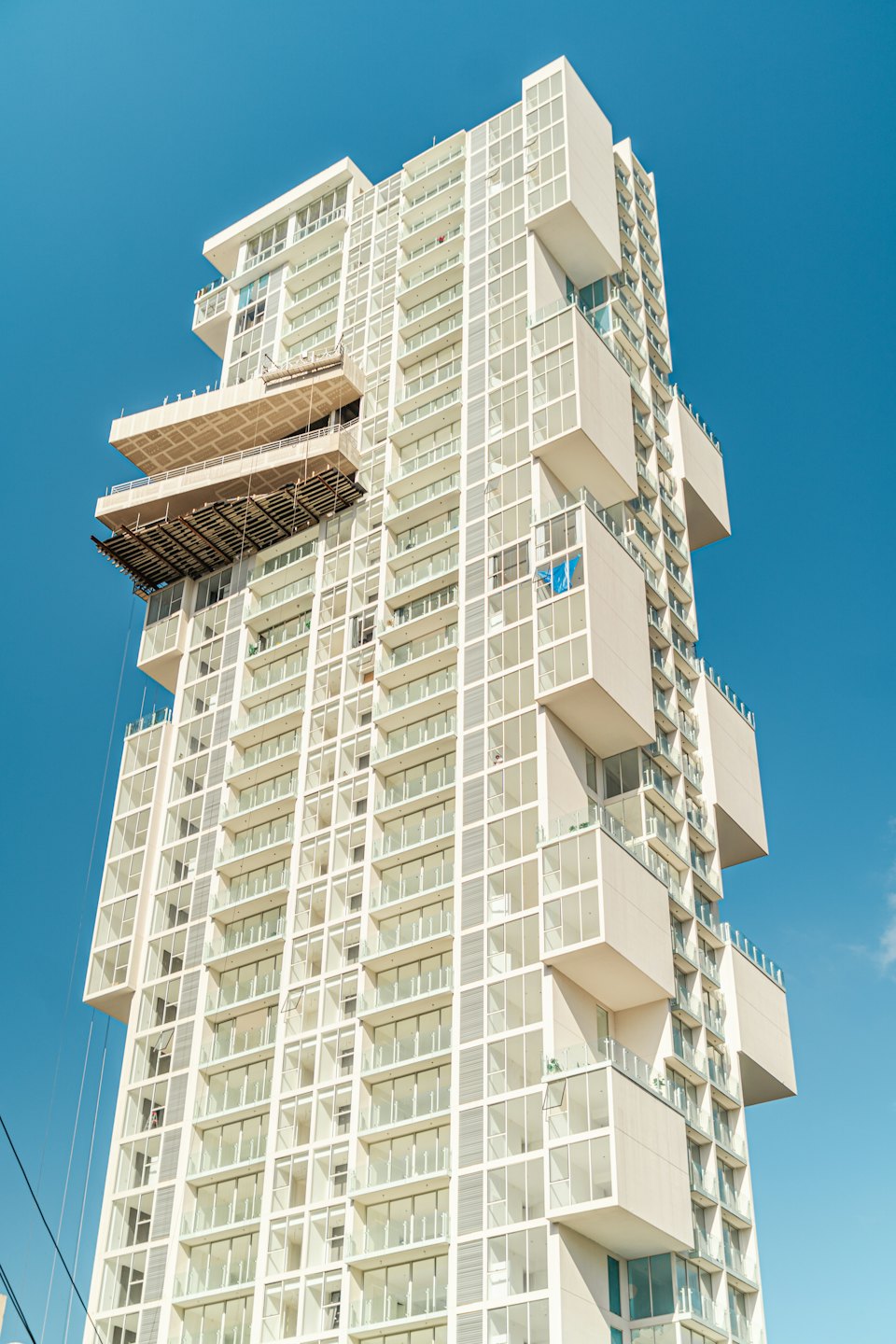 Modern white apartment building with scaffolding against blue sky.
