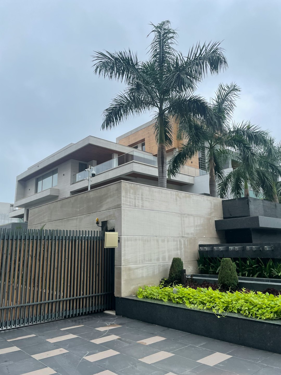 Modern multi-story house with concrete walls and palm trees.
