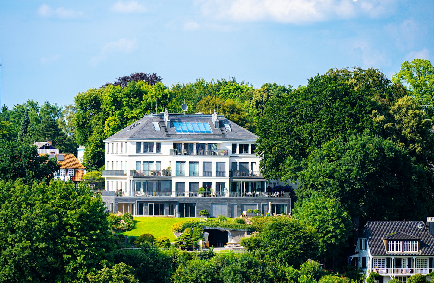 Modern white residential building sitting on a green landscaped hill.